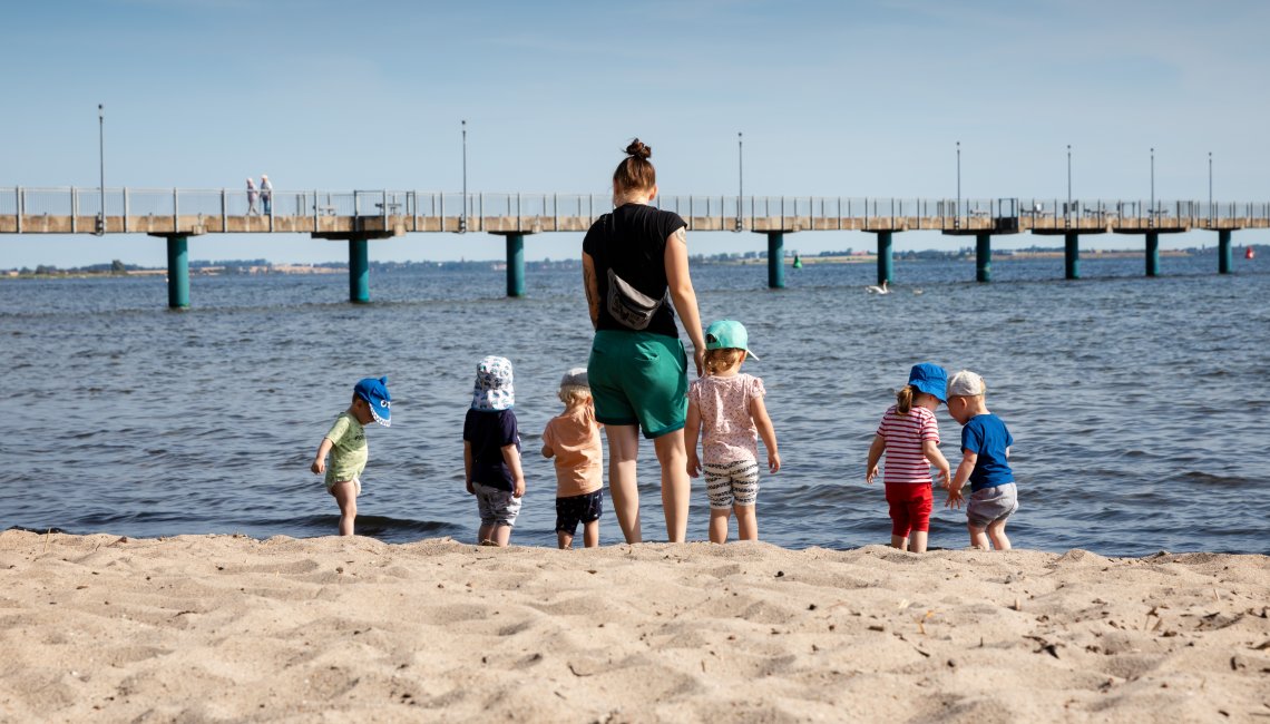 Eine Erzieherin und mehrere Kinder spielen am Strand.