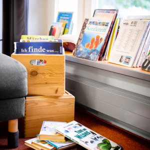 B&uuml;cher liegen und stehen vor einem Fenster in einer Leseecke.